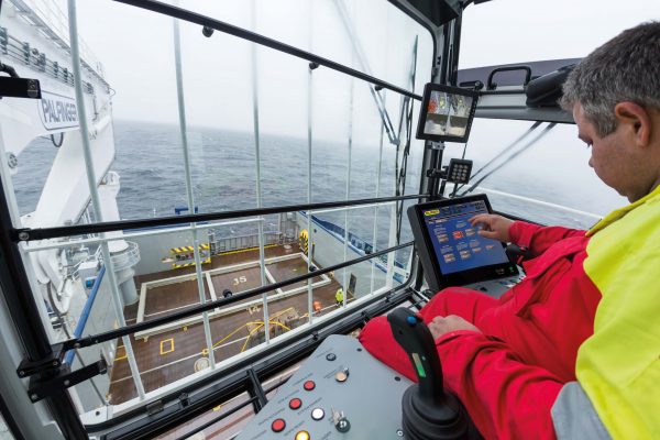 Man in a crane operator cabin on the deck of a vessel, making settings via a touch display