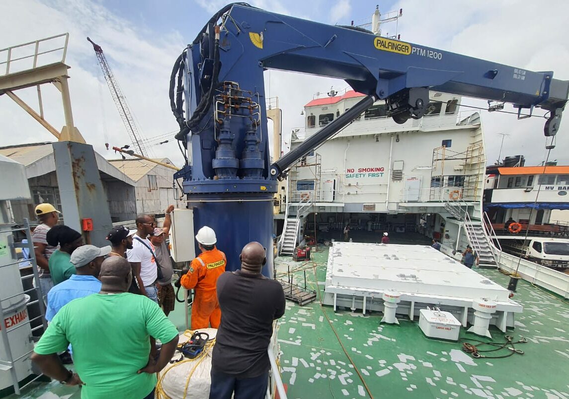 Group of men on a ship watching and listening to a marine crane operator, who is conducting a training